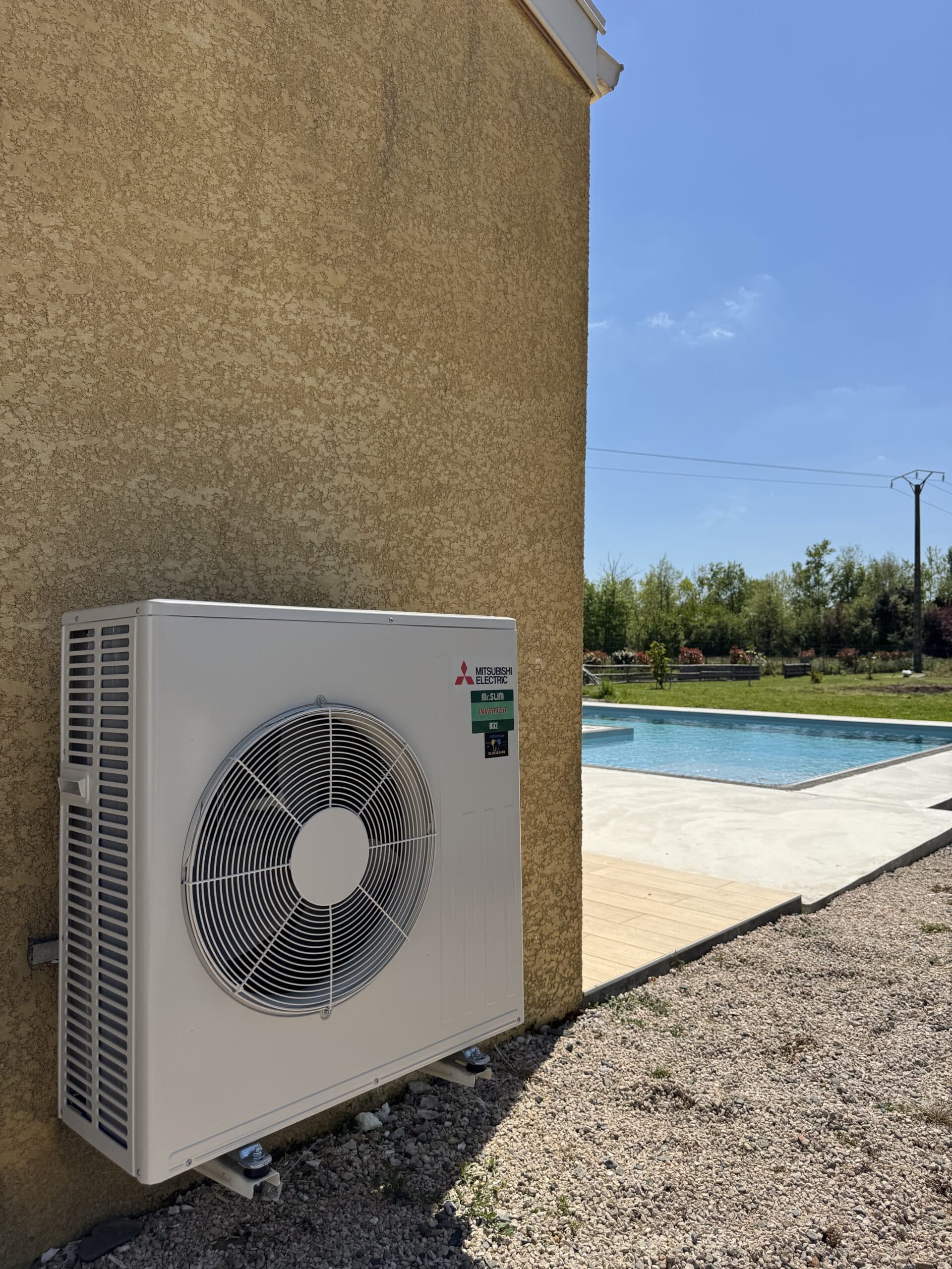 Climatiseur mural blanc moderne au-dessus d'un canapé gris clair, avec la lumière du soleil filtrant par une grande fenêtre. Ambiance intérieure lumineuse.