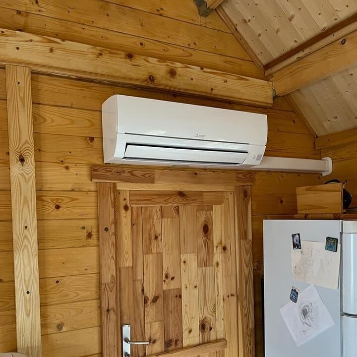 Climatiseur Mitsubishi mural blanc installé au-dessus d'une porte en bois rustique dans un intérieur lambrissé de bois clair.