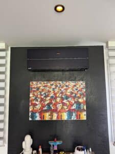 Climatiseur noir Mitsubishi Electric au-dessus d'une peinture vibrante de toits colorés sur un mur texturé anthracite.