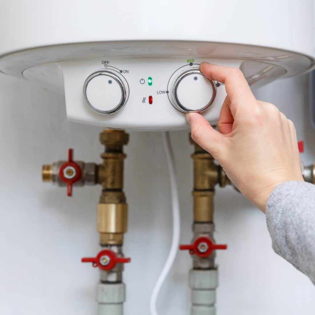 Ajuster le réglage Éco du thermostat d'un chauffe-eau Main ajustant le thermostat d'un chauffe-eau électrique sur la position 'ECO', avec voyants 'ON' (vert) et chauffage (rouge).